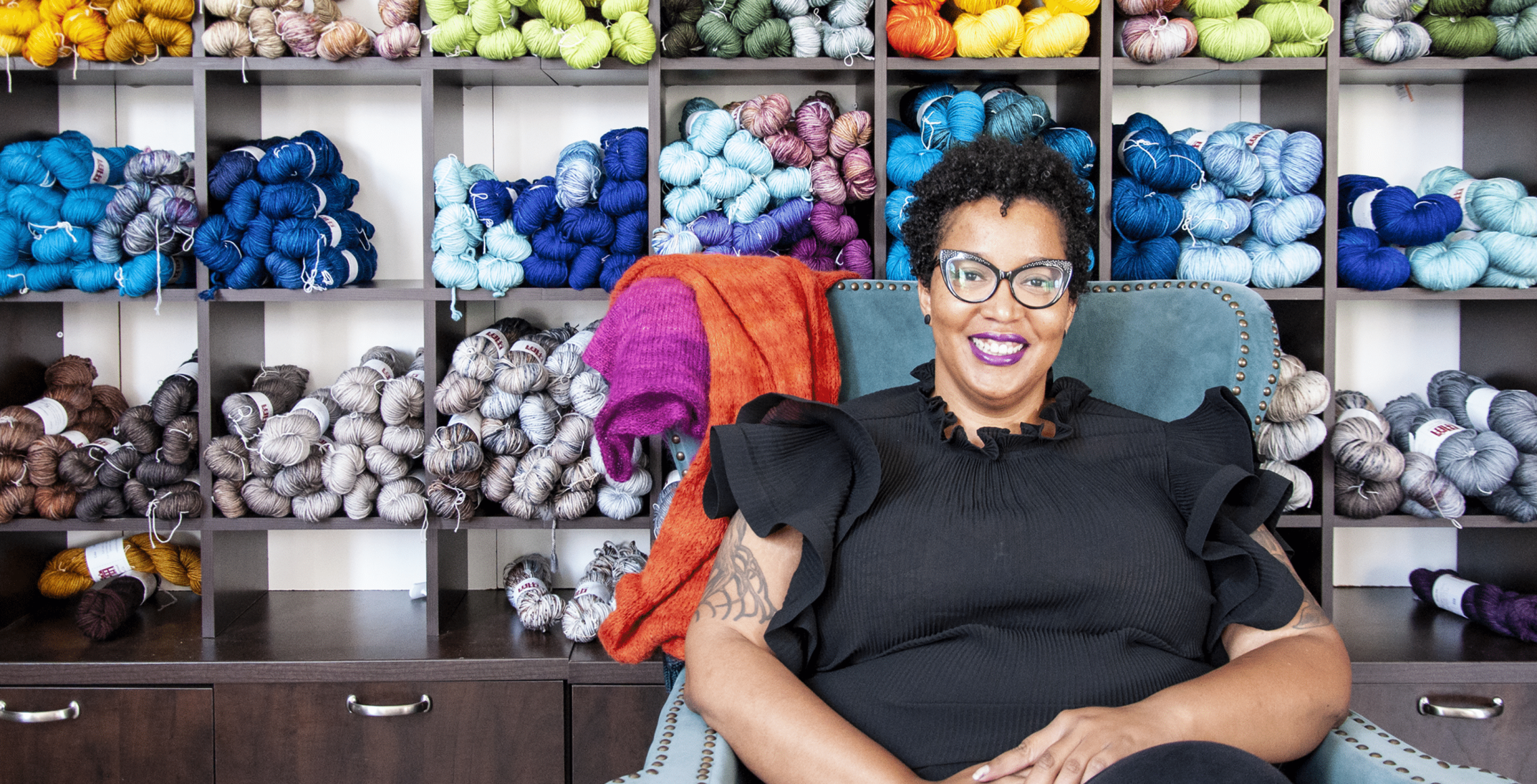 Woman sitting in front of shelves full of yarn