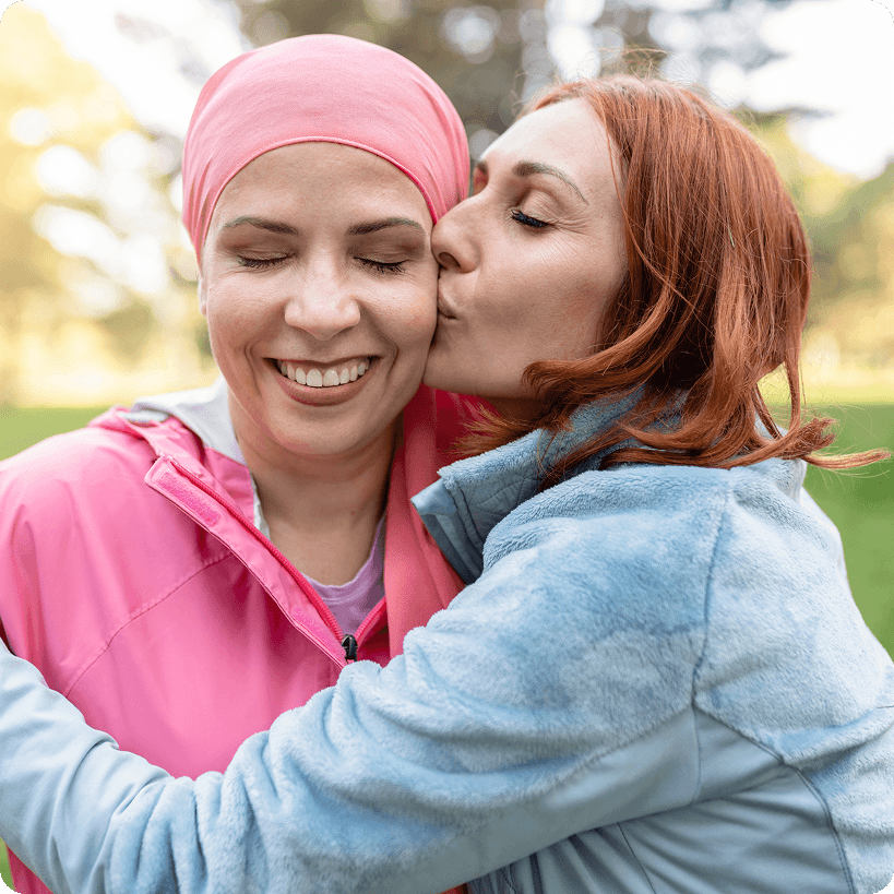 A friend giving her friend who has breast cancer a kiss on the cheek